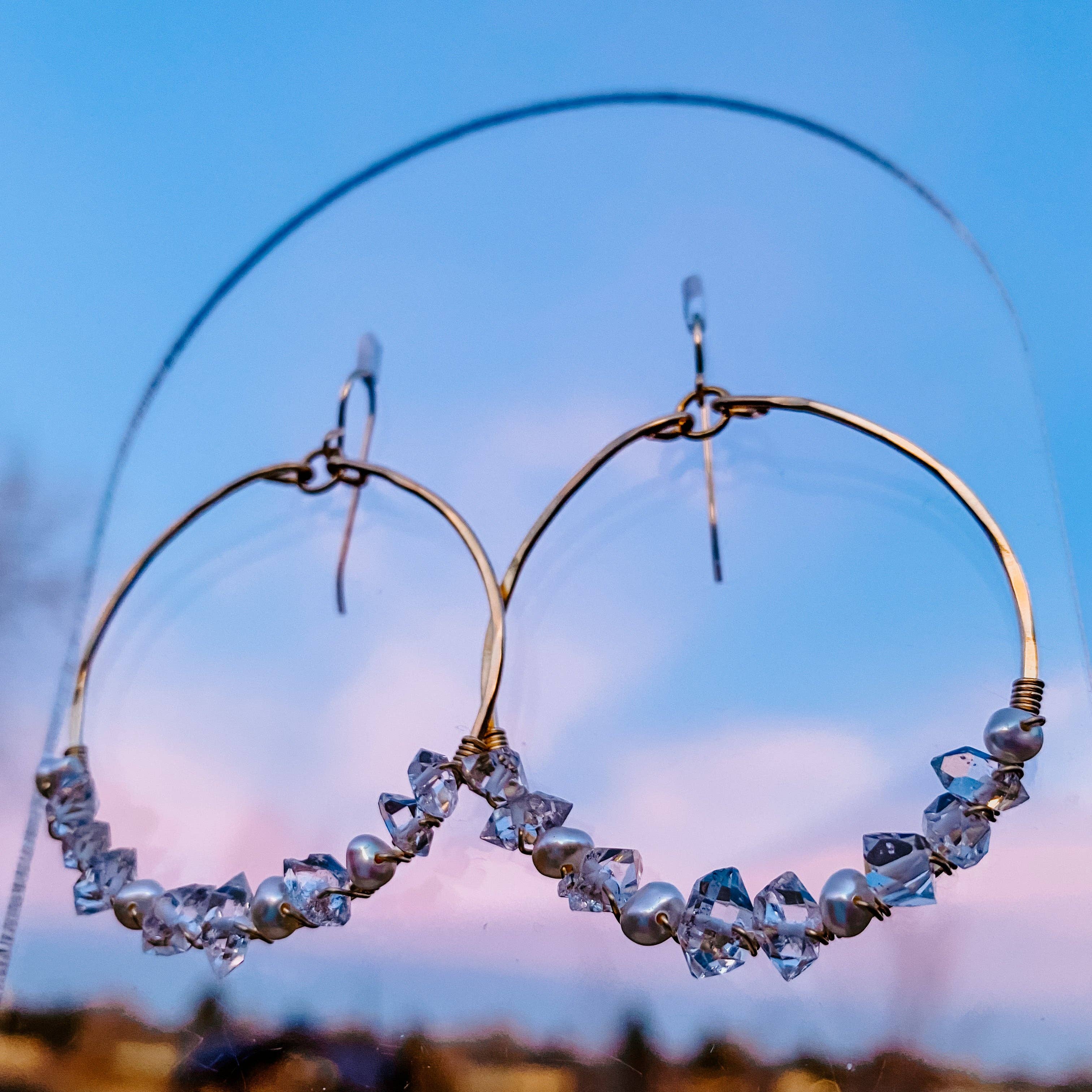 Close-up view of Everly Herkimer Diamond and Pearl Hoop Earrings by Derive Jewelry, showcasing the unique clarity of Herkimer diamonds and freshwater pearls against a sunset background.