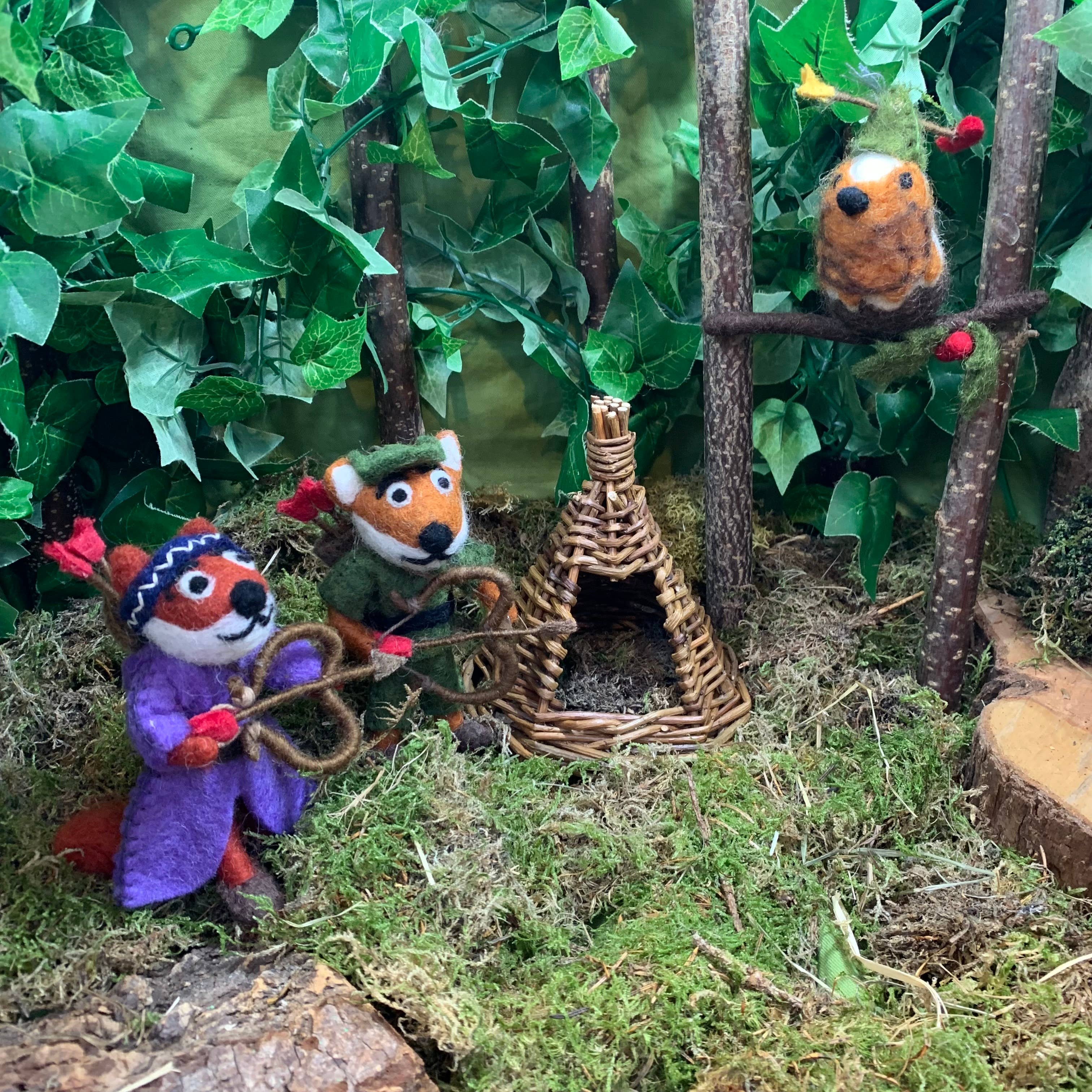 Felt animal ornaments in a forest setting with a small woven house.