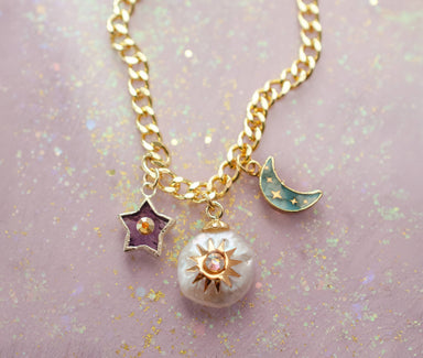 Artistic view of the Pearl and Moon Celestial Charm Necklace by Jill Makes, showcasing the gold charms including a pearl sun, amethyst star, and the labradorite moon against a glittery background.