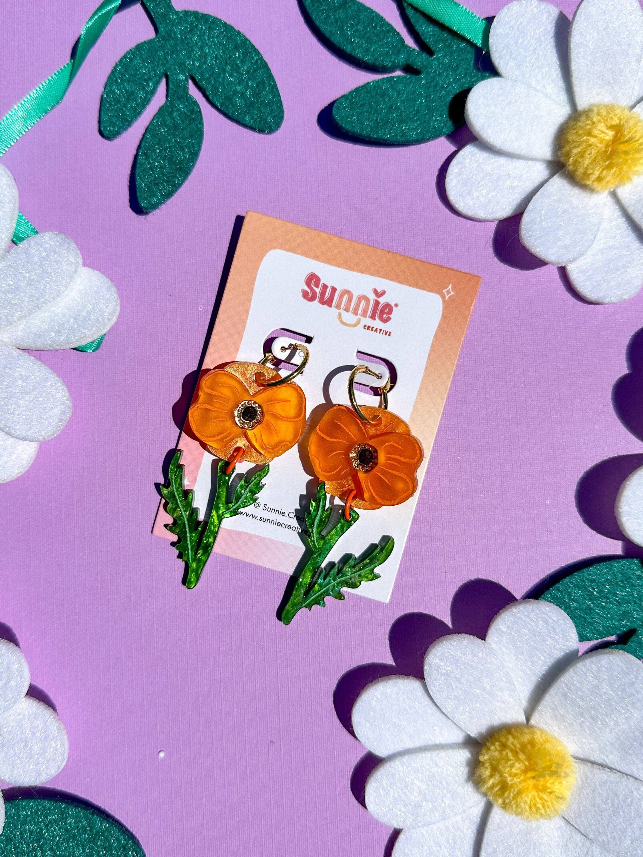 Poppy Bloom flower earrings by Sunnie Creative displayed on a colorful background with white felt flowers.