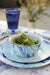 A beautifully set table featuring Crow Canyon Home Enamelware Lagoon Tasting Dishes, displaying a salad in a marbled bowl among blue accents, ideal for an elegant dining experience.