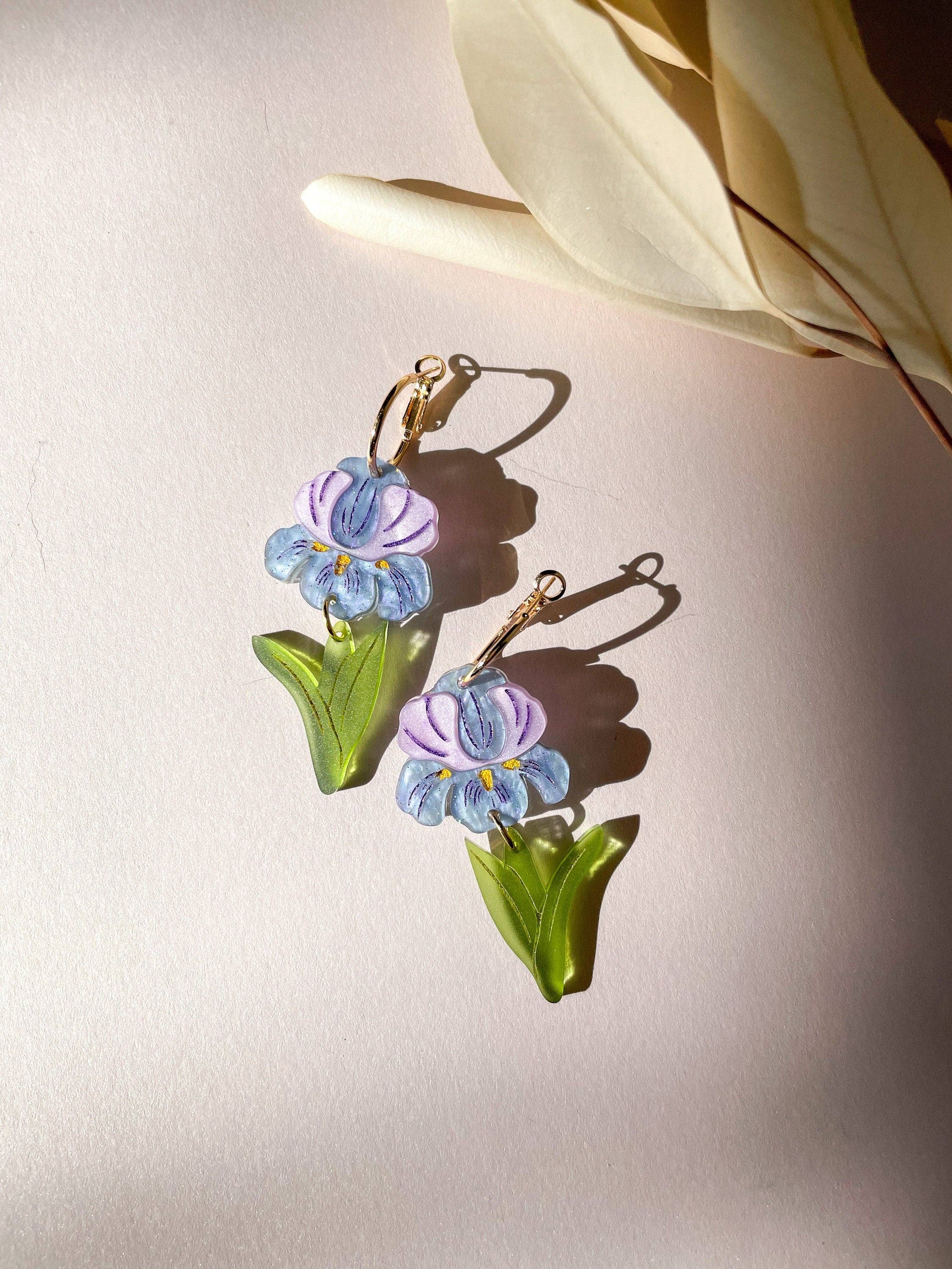 A close-up view of the Purple Iris earrings by Sunnie Creative, displayed on a soft background, highlighting the intricate flower design with vibrant colors and unique shape.