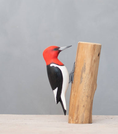 A hand-carved wooden woodpecker with a vibrant red head and belly by Aviologie, showcasing its craftsmanship in a natural setting.