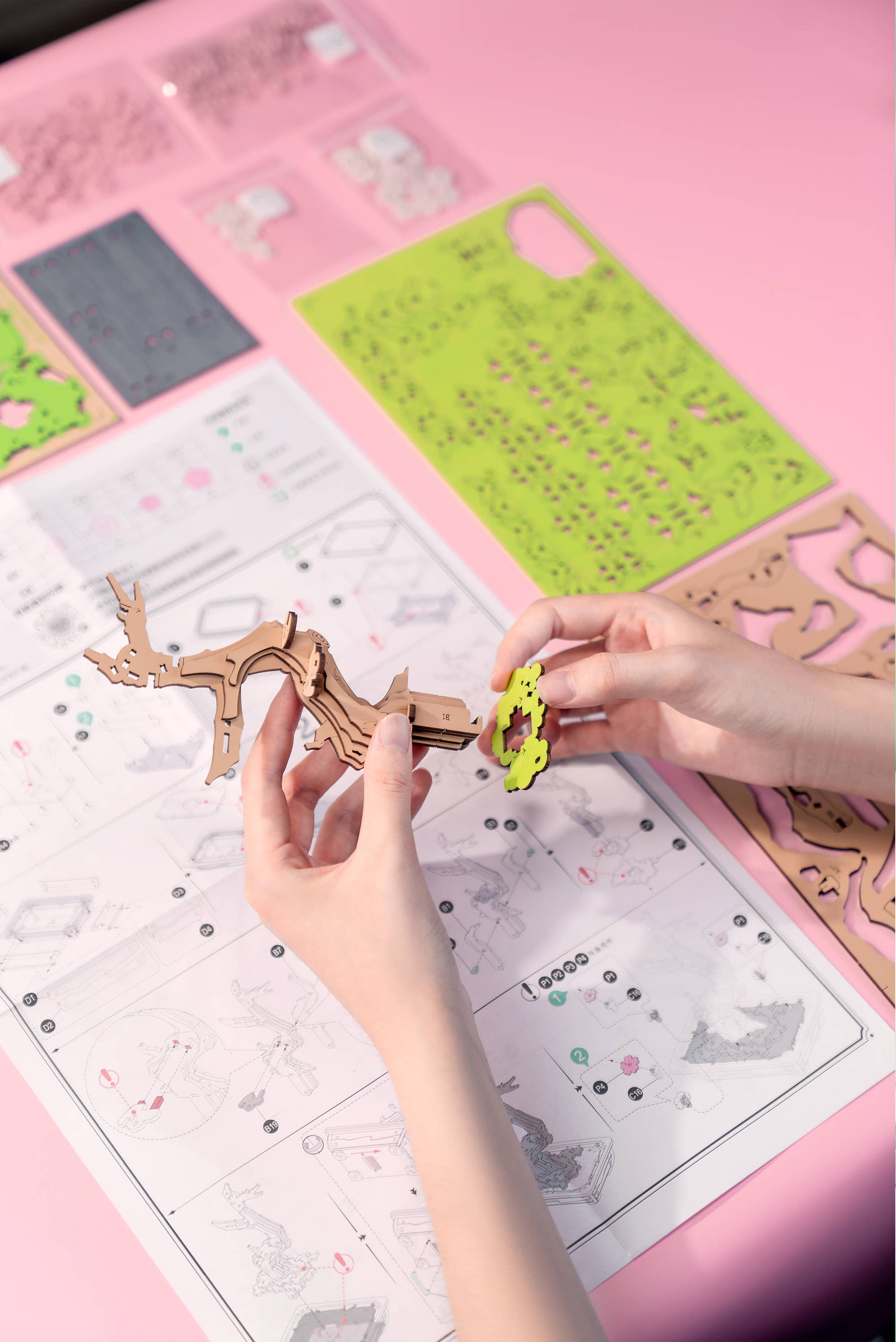 Hands Craft's Sakura Bonsai Modern Wooden Puzzle demonstrating the assembly process with hands working on precision-cut wooden pieces and a detailed instruction sheet.