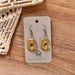 The Olive Square Loop Ceramic Stoneware Earrings displayed on a branded backing card from The Artifact House, highlighting their handmade elegance and 24K gold accents.