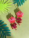Vibrant Hibiscus Dangle earrings by Sunnie Creative, featuring pink and purple floral designs with dangling accents, displayed against a green backdrop with tropical leaves.