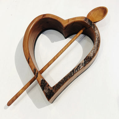 Handcrafted olive wood spoon suspended in a heart-shaped madrone wood frame, created by Hearts for the Arts for the item 'He Ran Out of Arrows'. This unique art piece showcases intricate woodwork and supports art education.