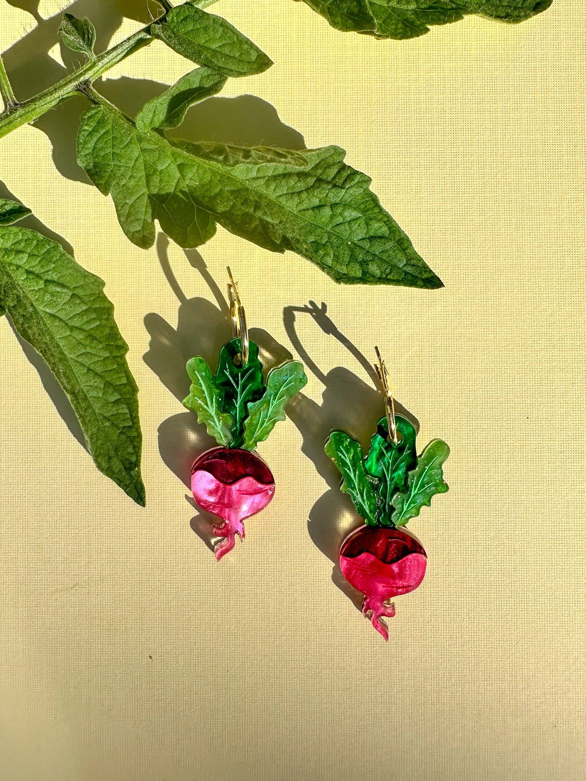 Ruby Radish Dangle earrings from Sunnie Creative, featuring vibrant pink radishes with green leaves, showcased against a light backdrop.