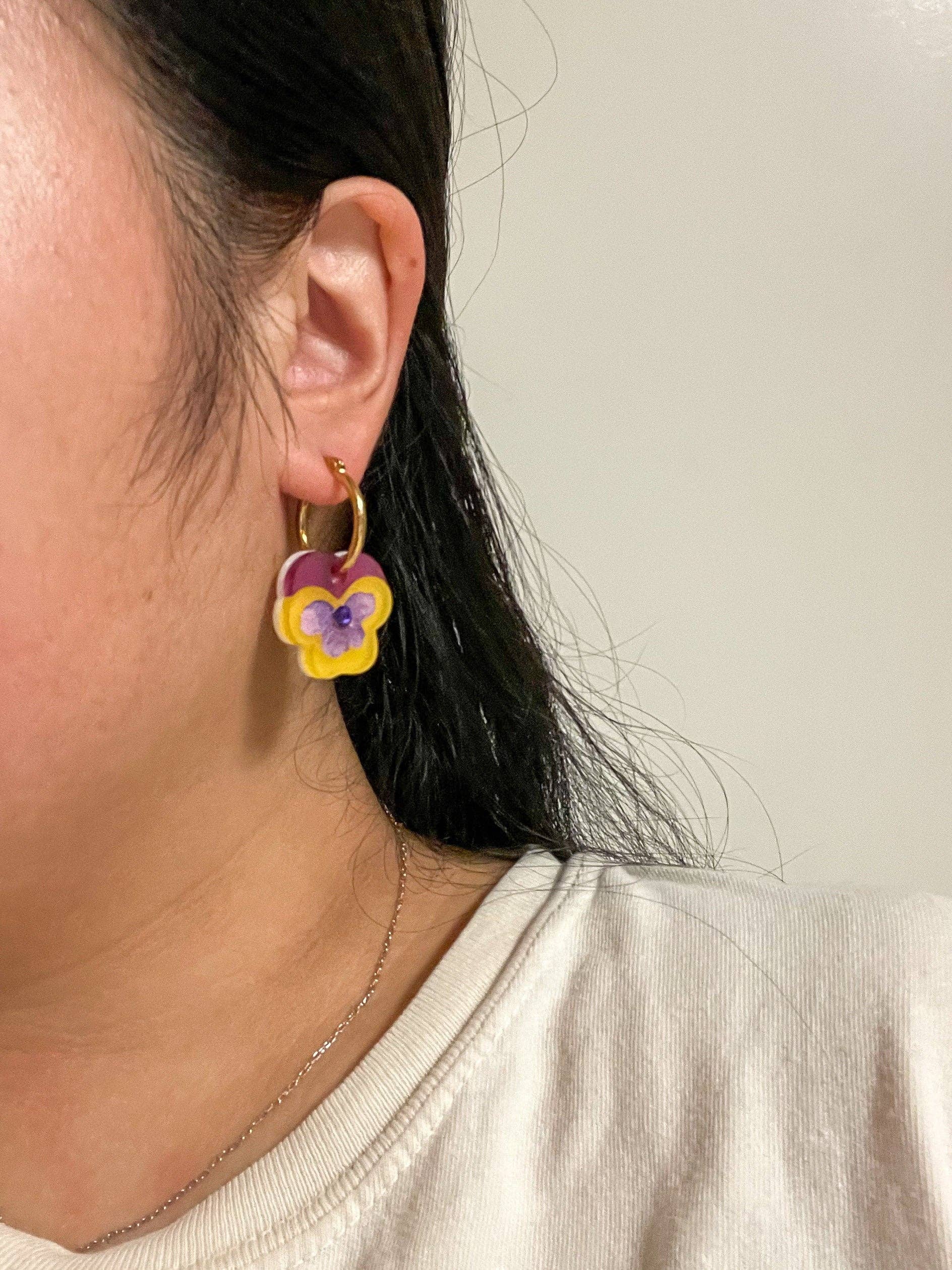 Close-up of a person wearing Mini Yellow Pansy Dangle earrings by Sunnie Creative, showcasing the vibrant yellow and purple floral design.
