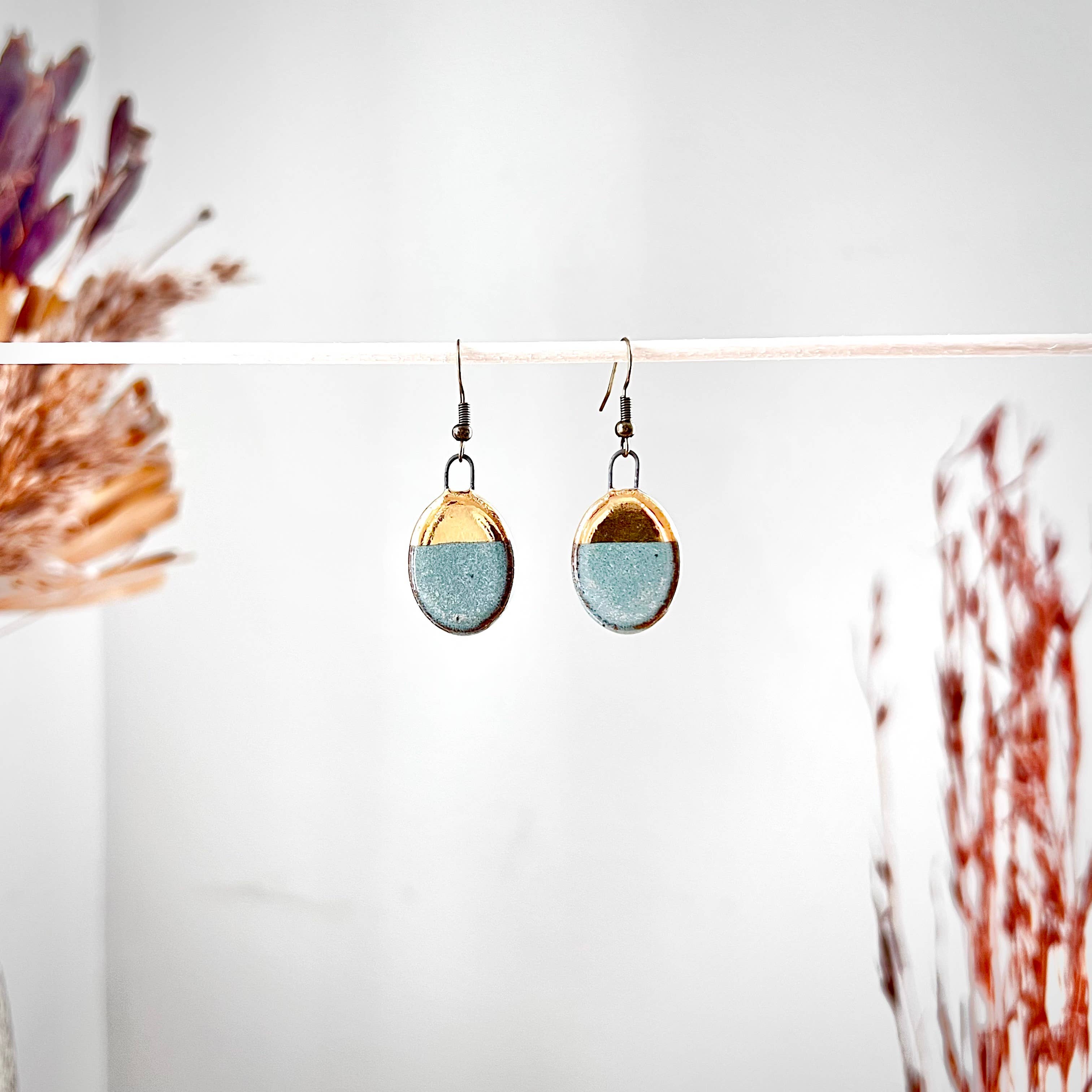 A close-up of Turquoise Dipped Oval Gold Earrings by The Artifact House, showcasing the beautiful blend of turquoise and gold on a chic display.