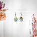 A close-up of Turquoise Dipped Oval Gold Earrings by The Artifact House, showcasing the beautiful blend of turquoise and gold on a chic display.