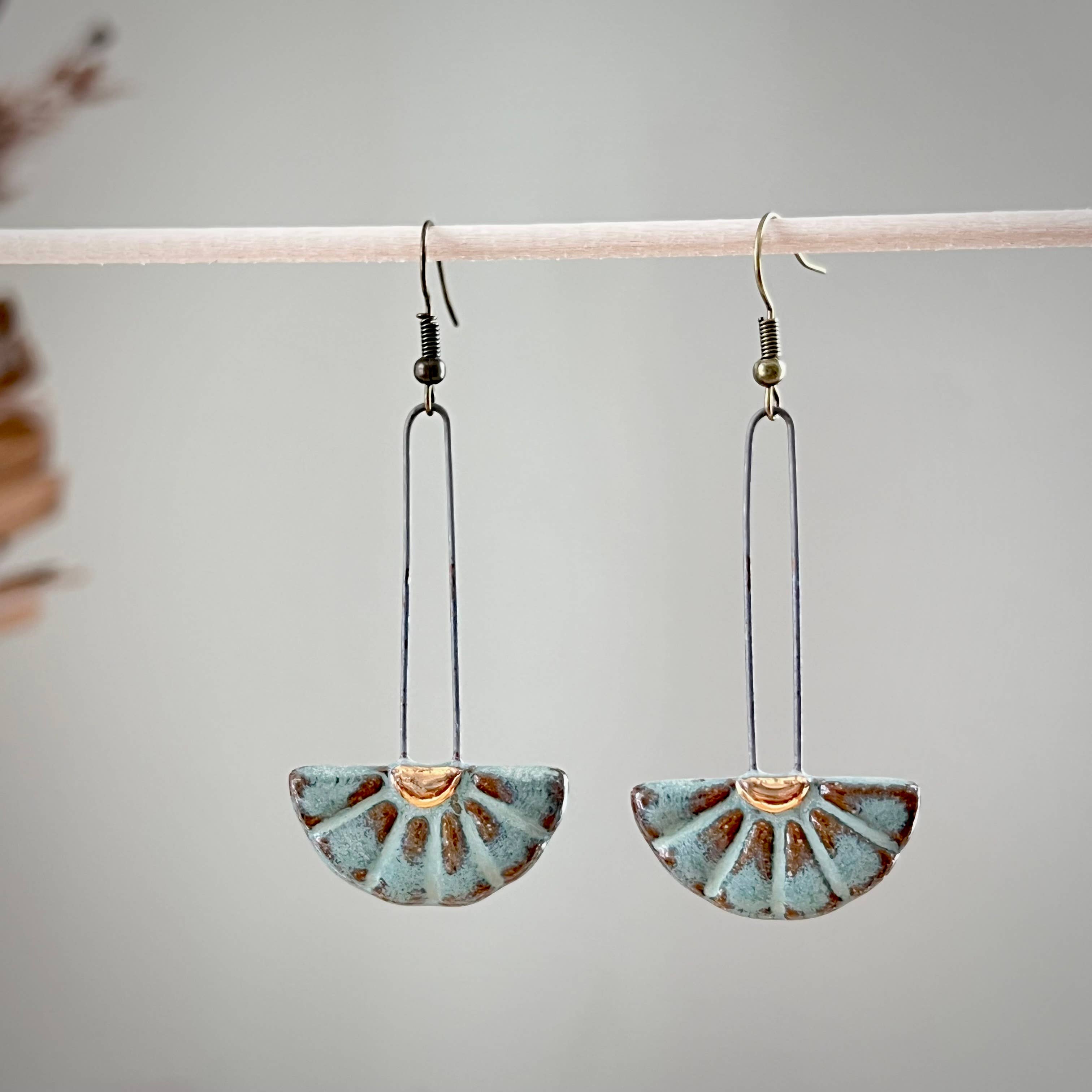 Turquoise Sun Burst Ceramic Earrings by The Artifact House hanging elegantly against a neutral backdrop, showcasing their unique sun burst design.