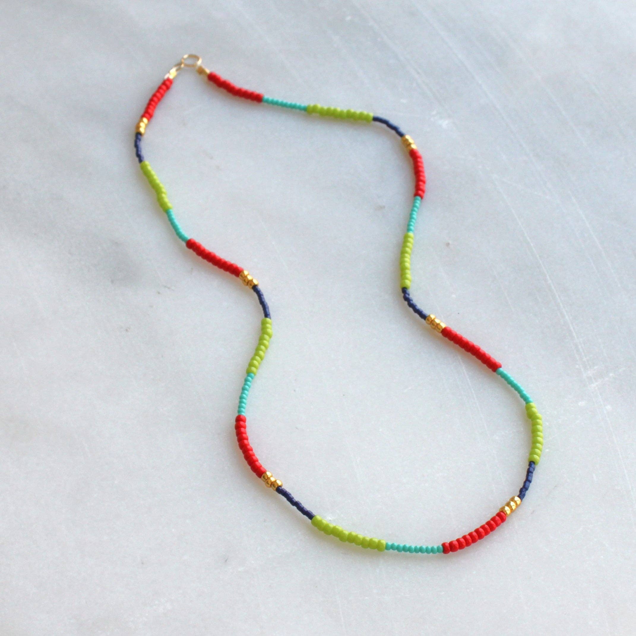 Flat lay image of the Lettie Seed Bead Necklace by The Silver Wren featuring bright red, green, and blue seed beads with gold accents.