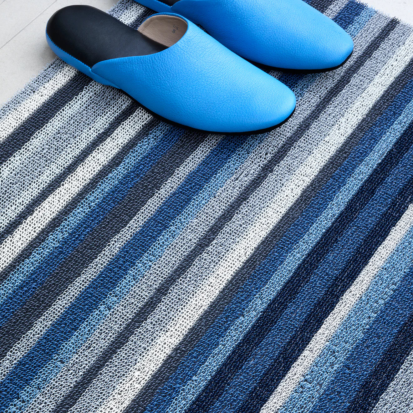 Lifestyle image of the Horizon Stripe Shag Mat in Deep Sea by Chilewich, showing its modern design and versatility in various home environments.