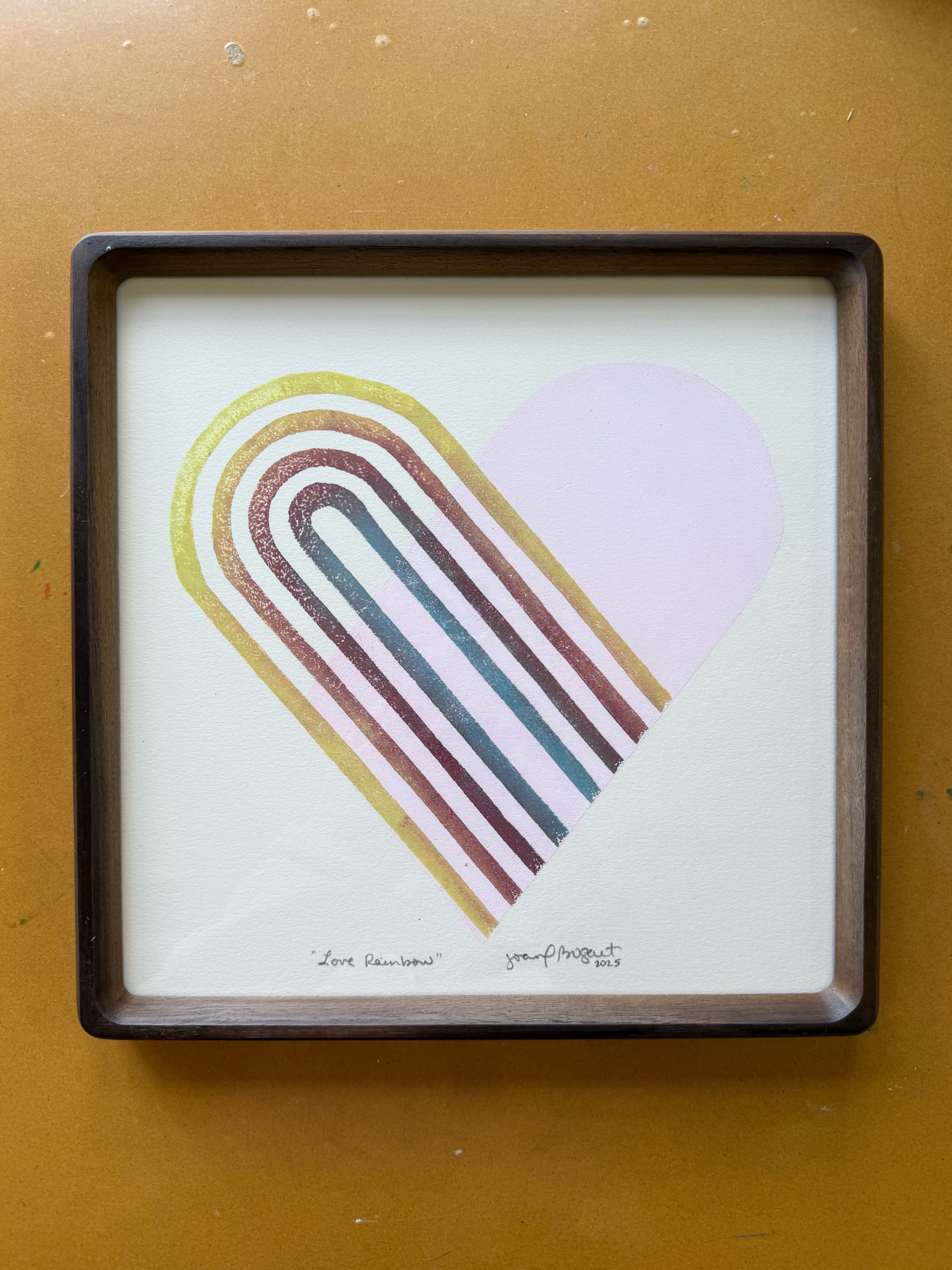 Block print artwork titled 'Love Rainbow' by Joan Bogart, featuring a colorful heart design with vibrant rainbow arches. Created by Hearts for the Arts, this 10x10 inch hand-carved piece emphasizes art education support.