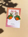 Mini Orange Dangle earrings by Sunnie Creative showcased on a branded card, highlighting their unique orange fruit design and hypoallergenic features, set on a light pastel background.
