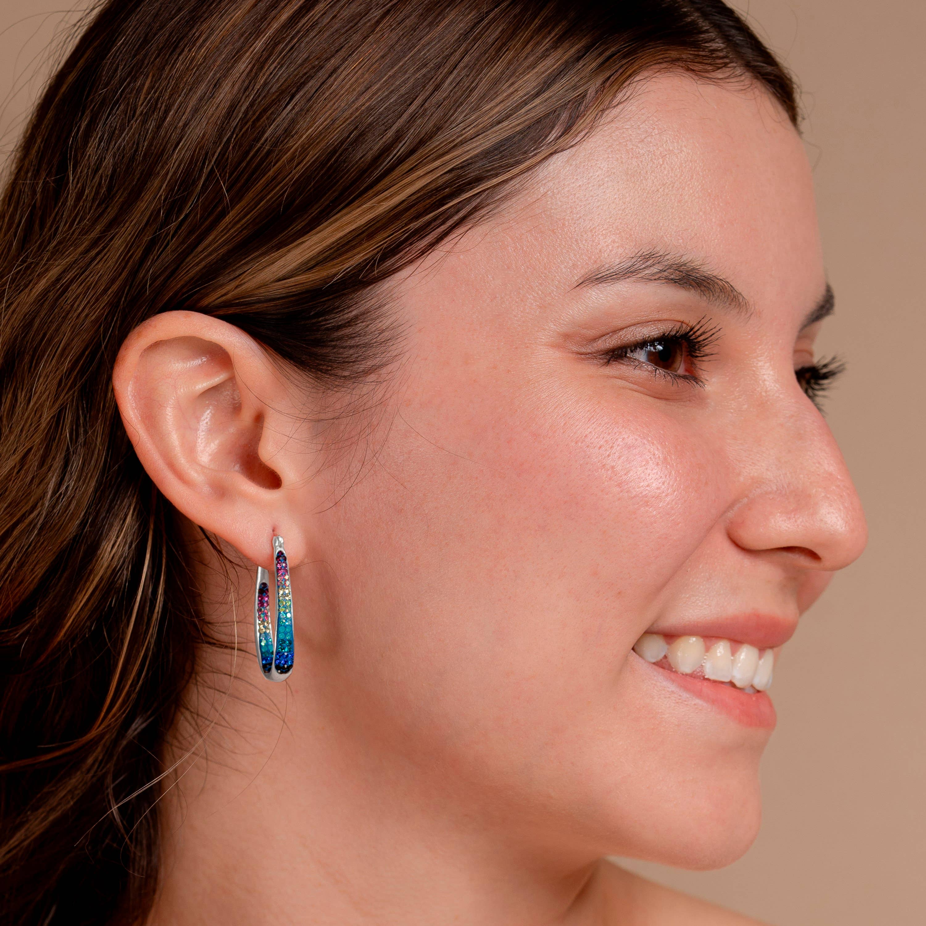 Model wearing Crystal Hoop Earrings by Mosaico Jewels, displaying the earrings' stunning design and colorful sparkle against a neutral background.