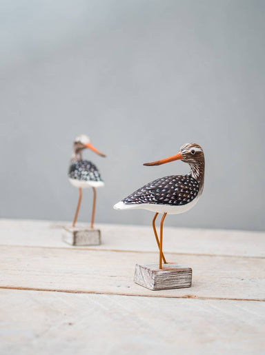 Mini Yellow Legs wooden ornament by Aviologie, showcasing intricate hand-carving and vibrant painting, displayed on a rustic wooden base.