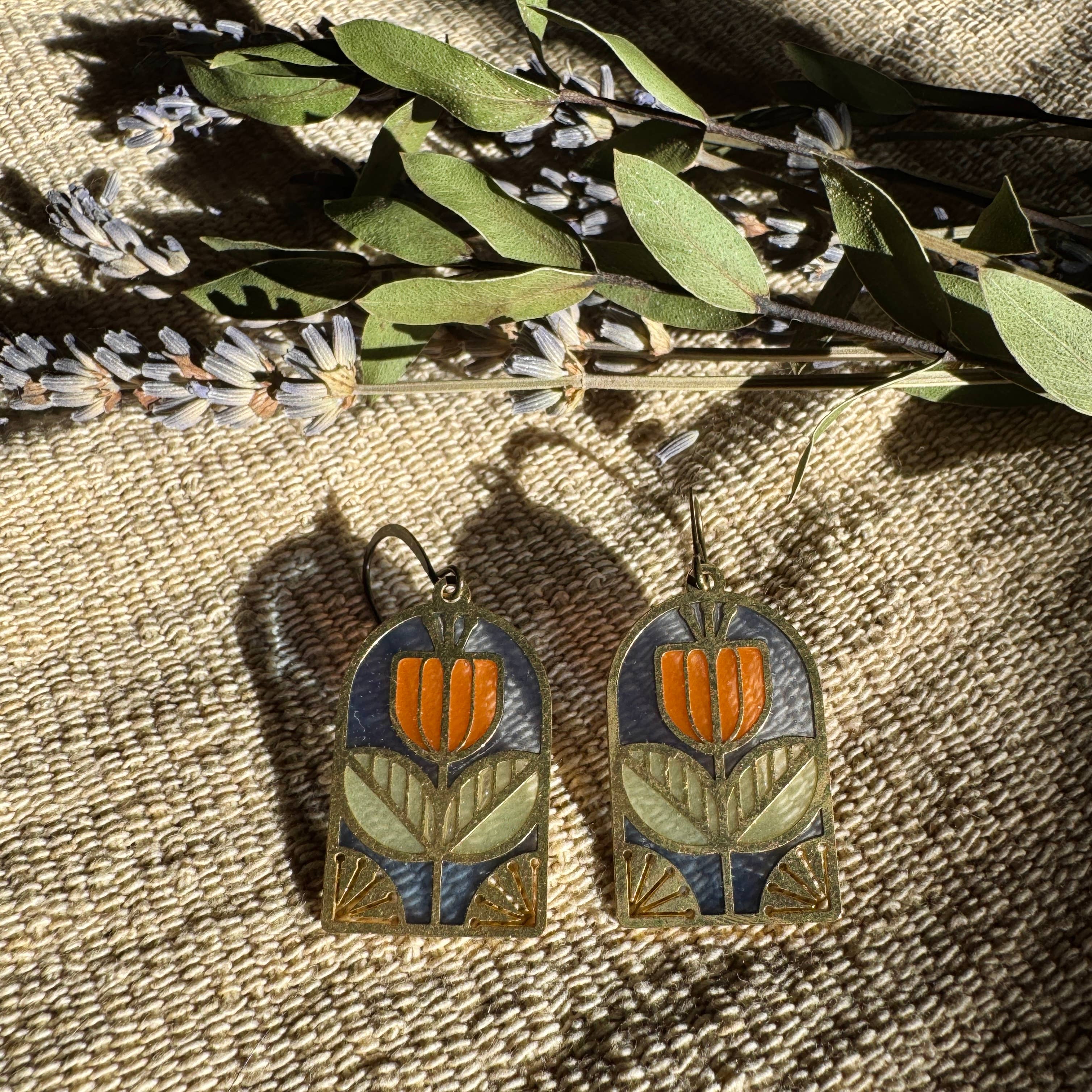 Tracery Stained Glass Resin Earrings by Wild Lupine Folkcraft showcased against a textured background, highlighting the brass geometric botanical design and soft-colored resin stained glass.