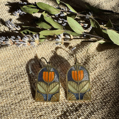Tracery Stained Glass Resin Earrings by Wild Lupine Folkcraft showcased against a textured background, highlighting the brass geometric botanical design and soft-colored resin stained glass.