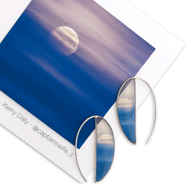 Moon Mist Long Crescent Earrings by Foterra Jewelry showcasing delicate crescent design with a scenic backdrop of the moon in soft blue hues. Made from hypoallergenic sterling silver, these earrings are designed for elegance and comfort.