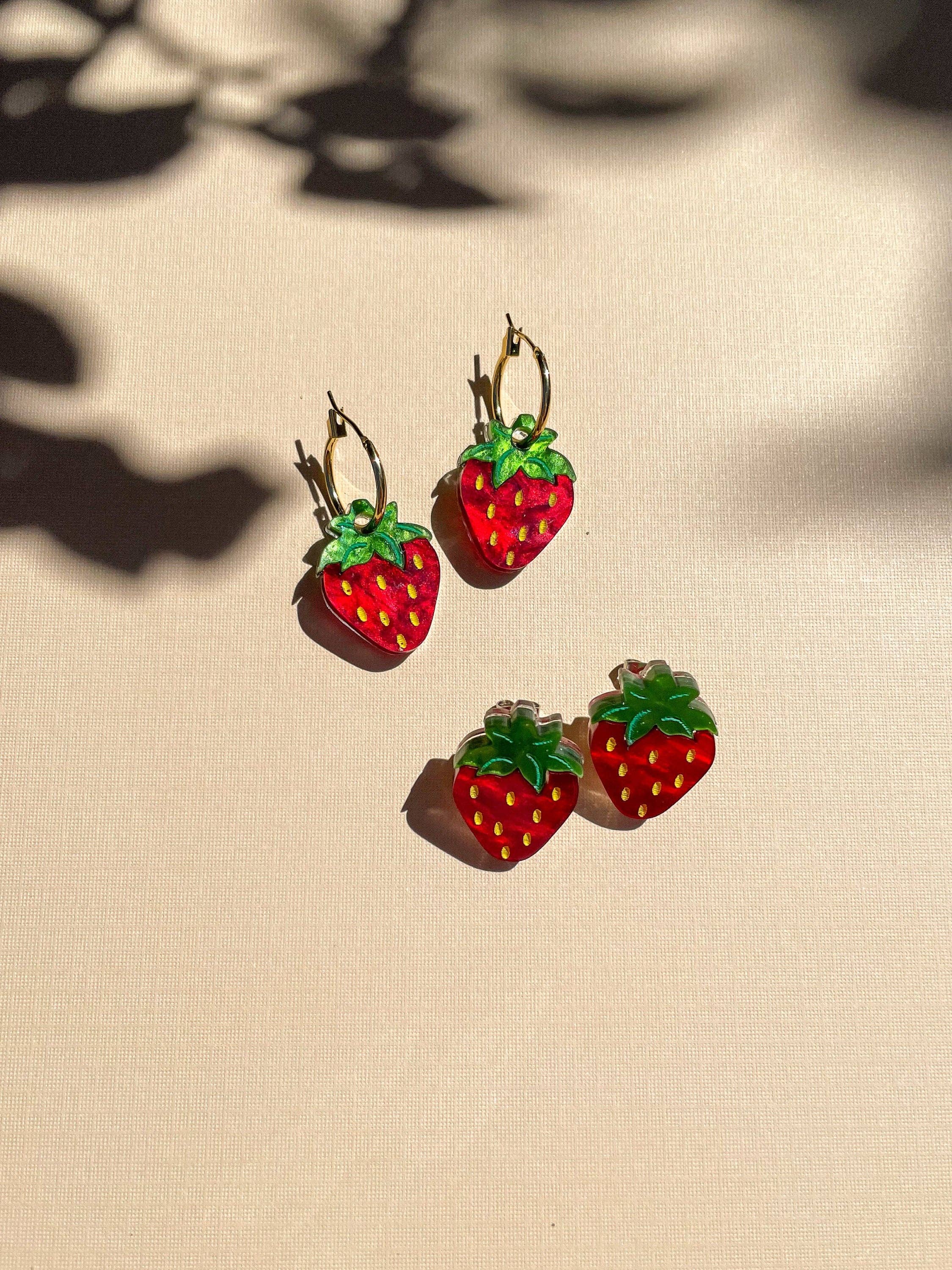 Mini Strawberry Acrylic Dangle Earrings by Sunnie Creative featuring vibrant red strawberries with green leaves, displayed in a natural light setting, highlighting their unique handmade design.