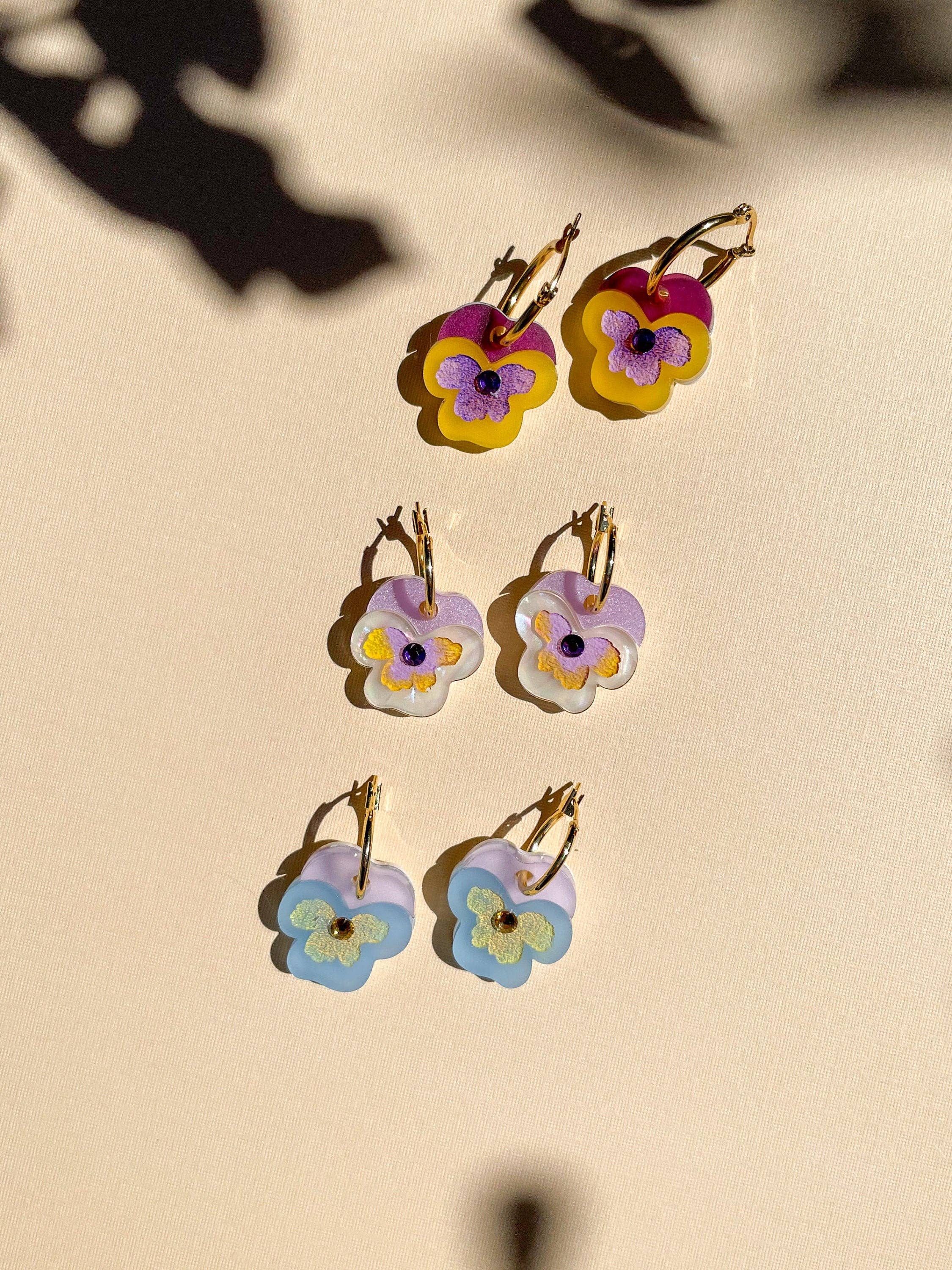 Handmade Mini Yellow Pansy Dangle earrings by Sunnie Creative, featuring unique colorful acrylic designs, displayed in a visually appealing arrangement against a soft background.