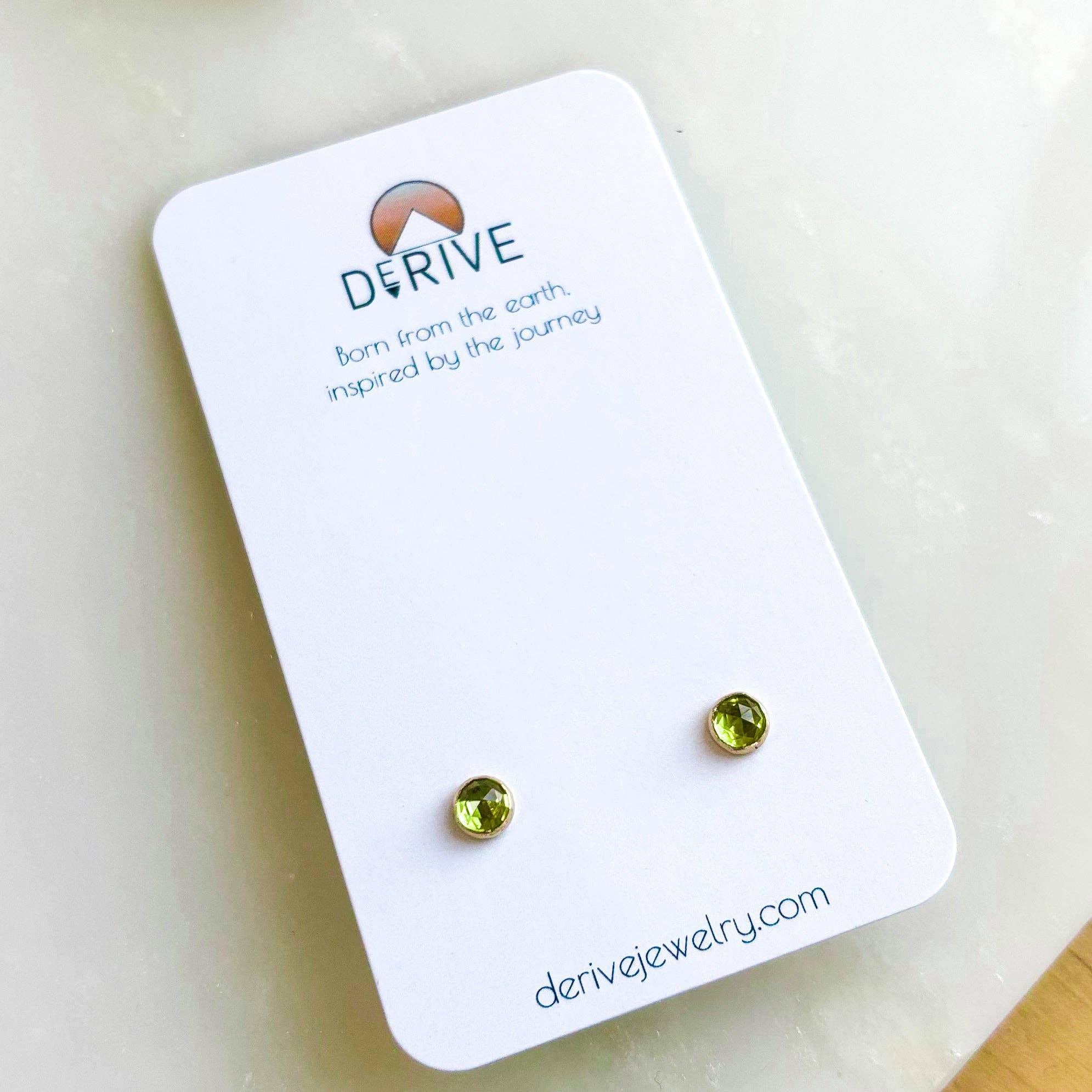 Single pair of Gemstone Stud Earrings from Derive Jewelry featuring a vibrant green Peridot gemstone on a display card.