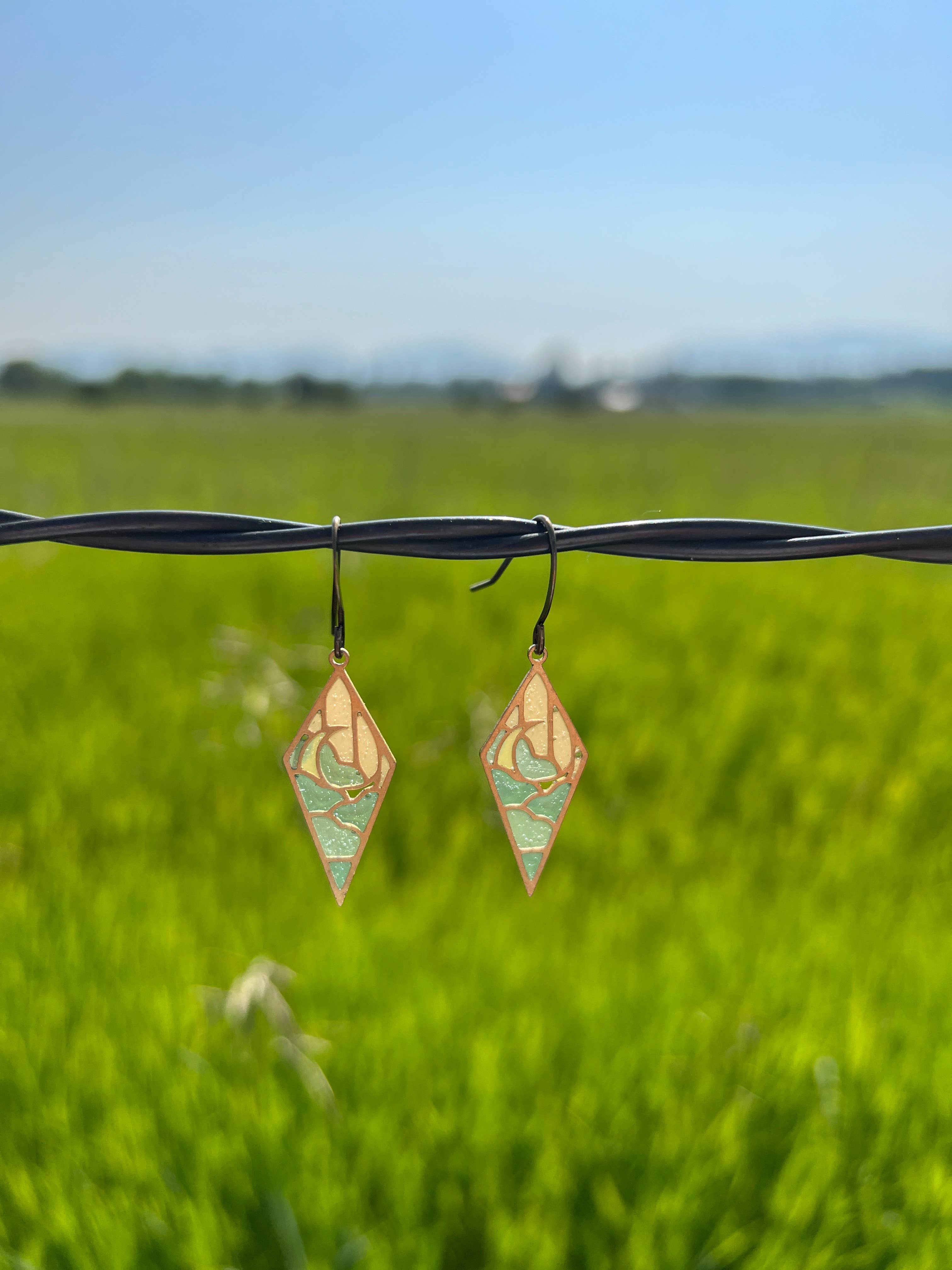 Moonrise Stained Glass Resin Earrings by Wild Lupine Folkcraft displayed against a vibrant green field background, showcasing their modern design and colorful stained glass effect.