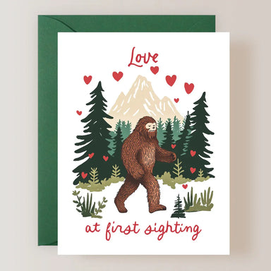 Illustration of a Bigfoot walking amidst tall trees and mountains, adorned with hearts, featured on a greeting card from the Firefly Paper Studio Card Collection.