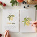 A person painting a page from the Fruit watercolor workbook, illustrating a fun and relaxing art experience.