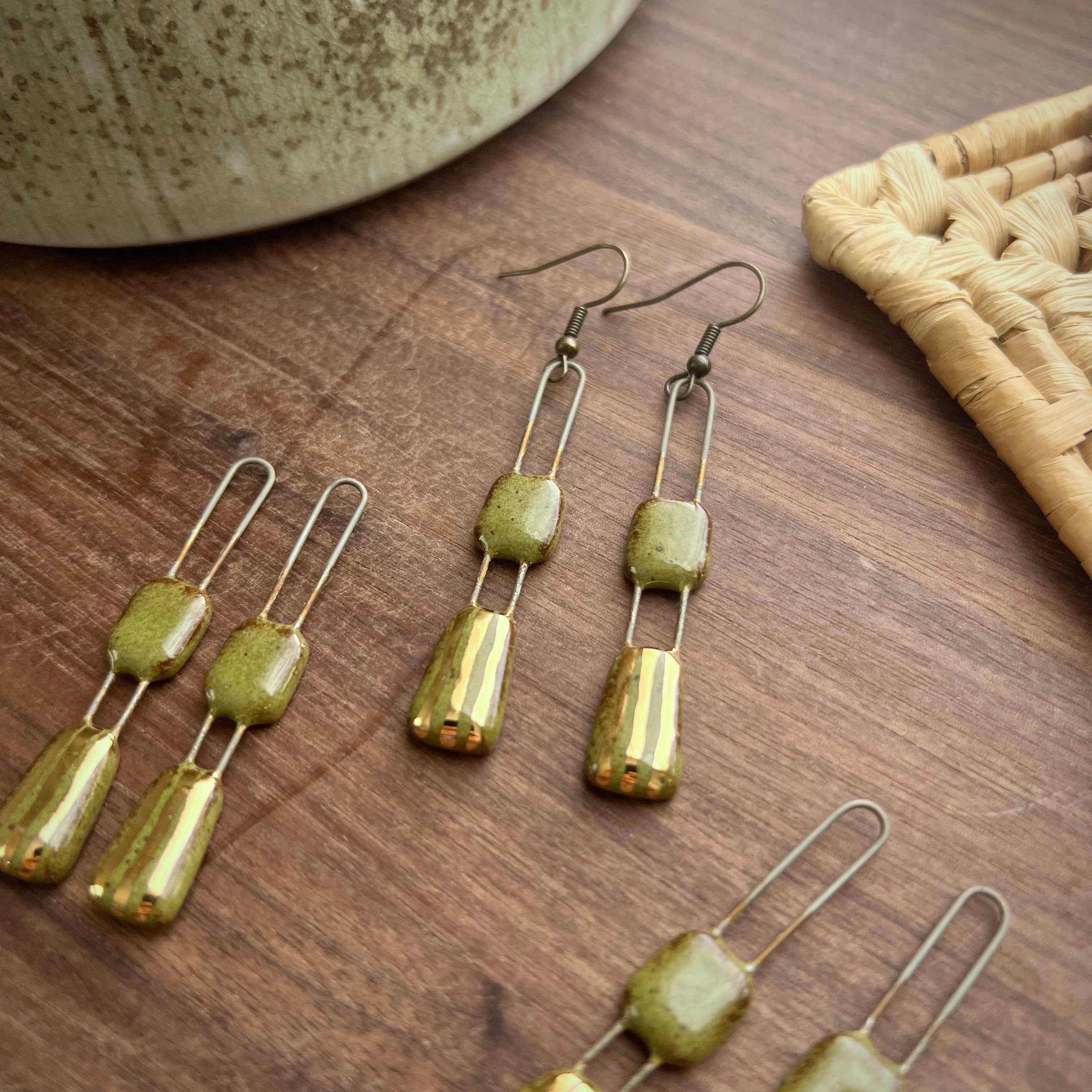 Close-up of Speckled Olive Two Piece Gold Lined Earrings by The Artifact House, showcasing details of the ceramic design on a wooden surface.