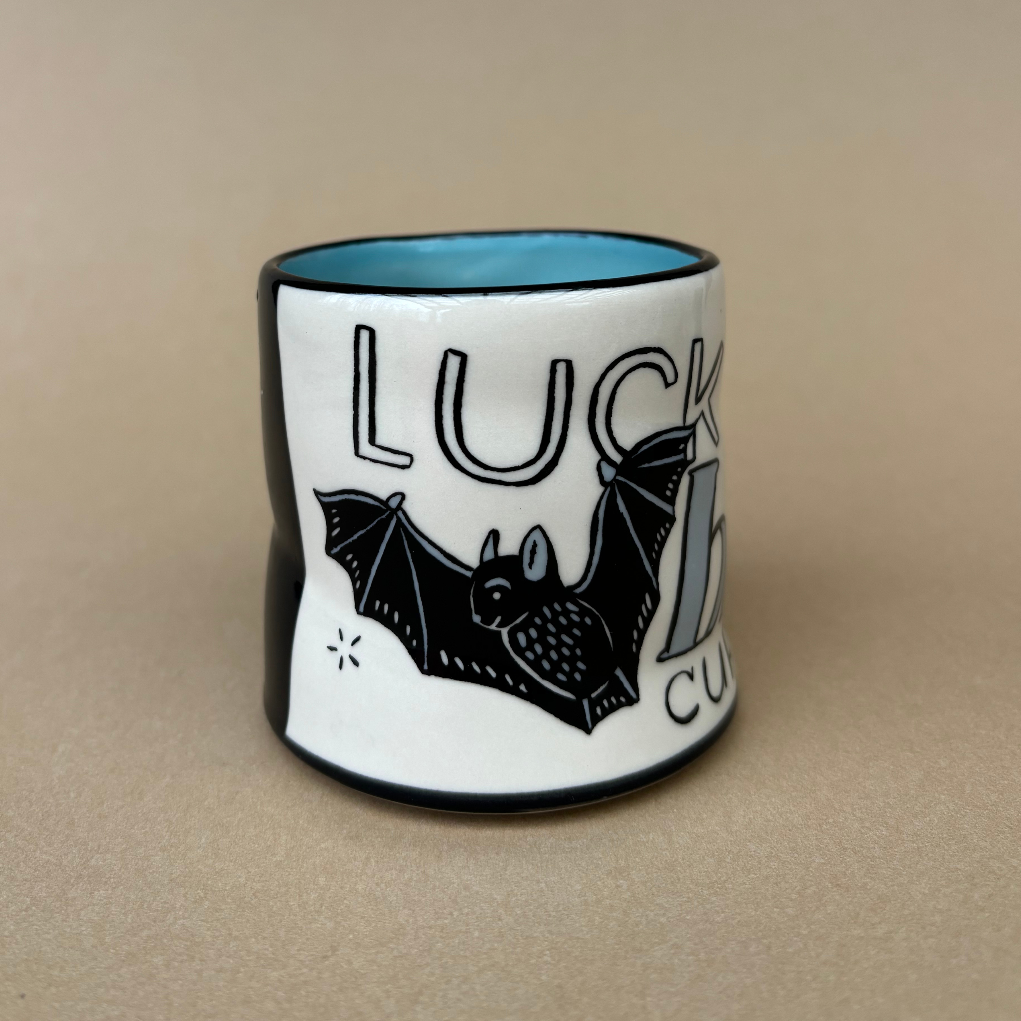Medium Lucky Bat Cup by The Bowl Maker, showcasing a whimsical illustration of a bat alongside the words 'Lucky Bat' on a smooth white surface.