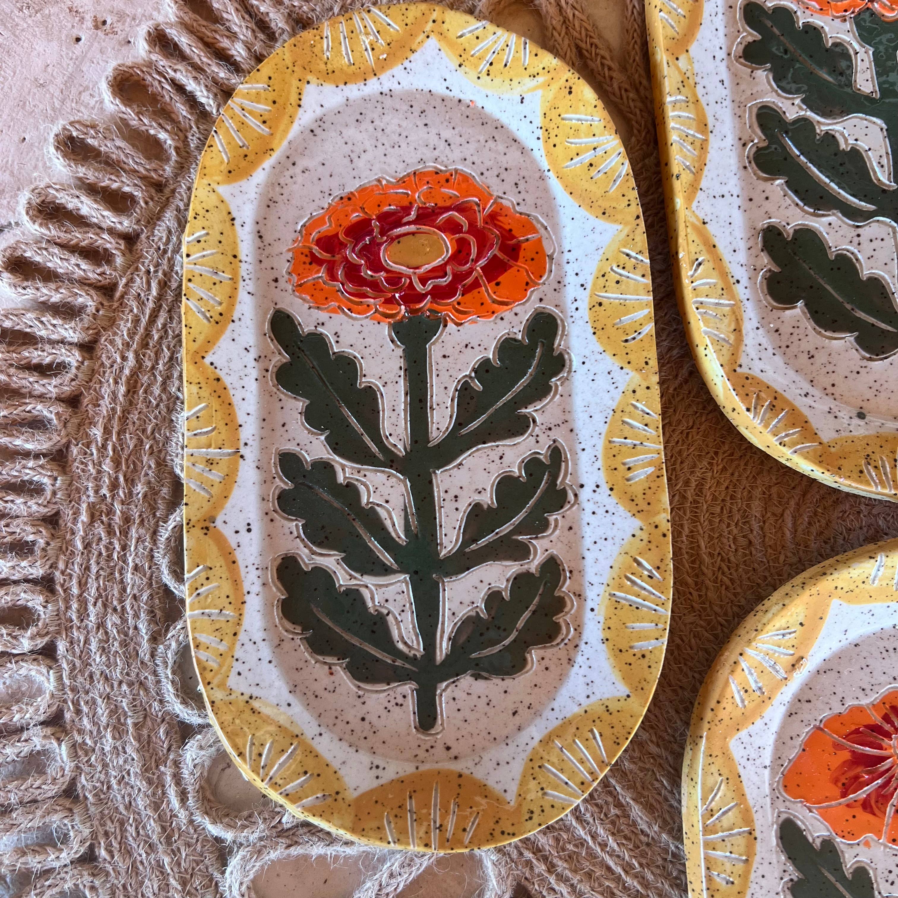 Close-up view of a single Marigold Ceramic Trinket Dish by Tough Kitty Designs, showcasing the intricate hand-cut and glazed marigold flower design in yellow and orange.