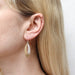 Close-up view of Medium Overlap Swoops Wire Earring by Marjorie Baer, showcasing the earring worn on the ear, highlighting its minimalist aesthetic and delicate wire backing.