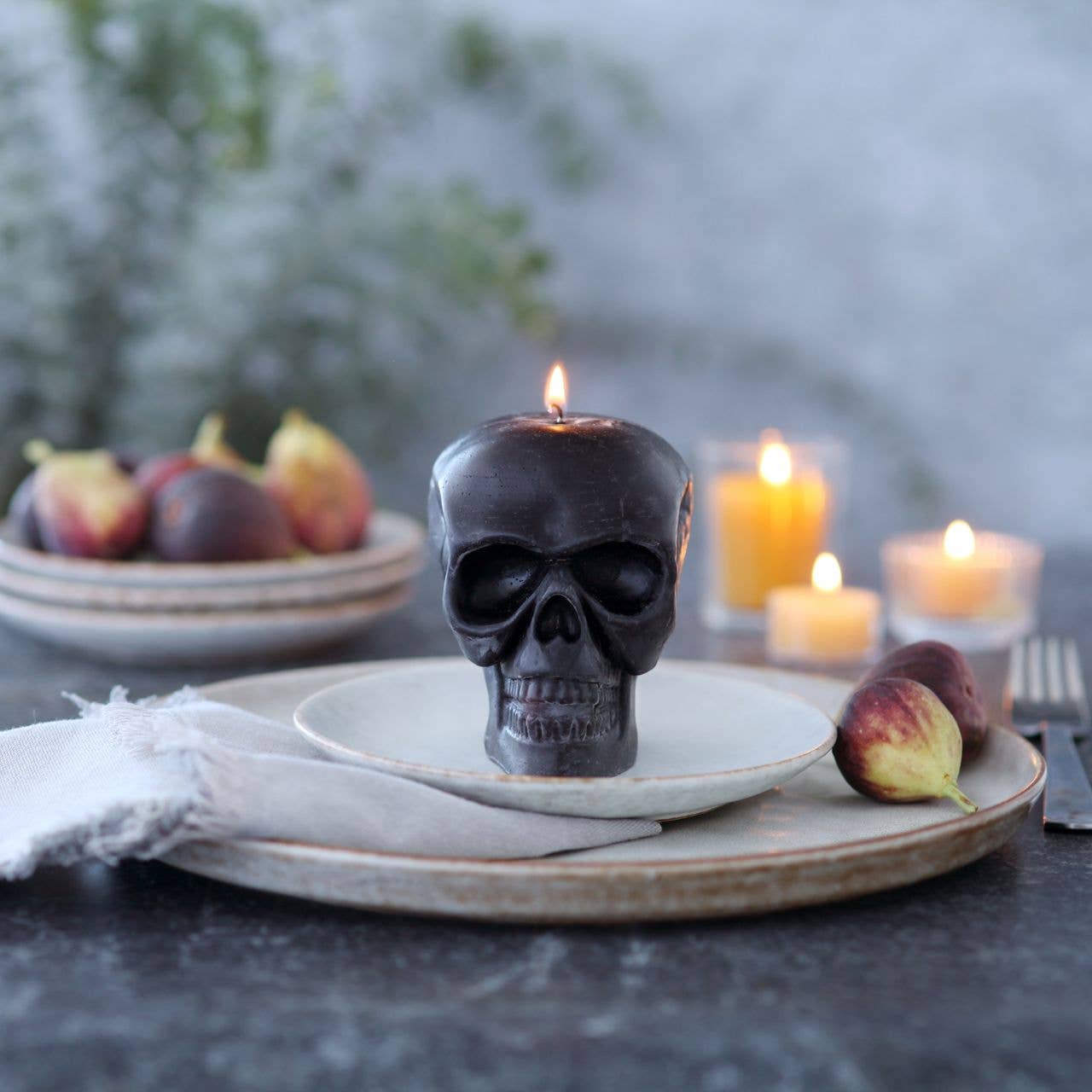 Skull-shaped candle on a plate with figs and other candles in the background