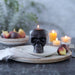 Skull-shaped candle on a plate with figs and other candles in the background