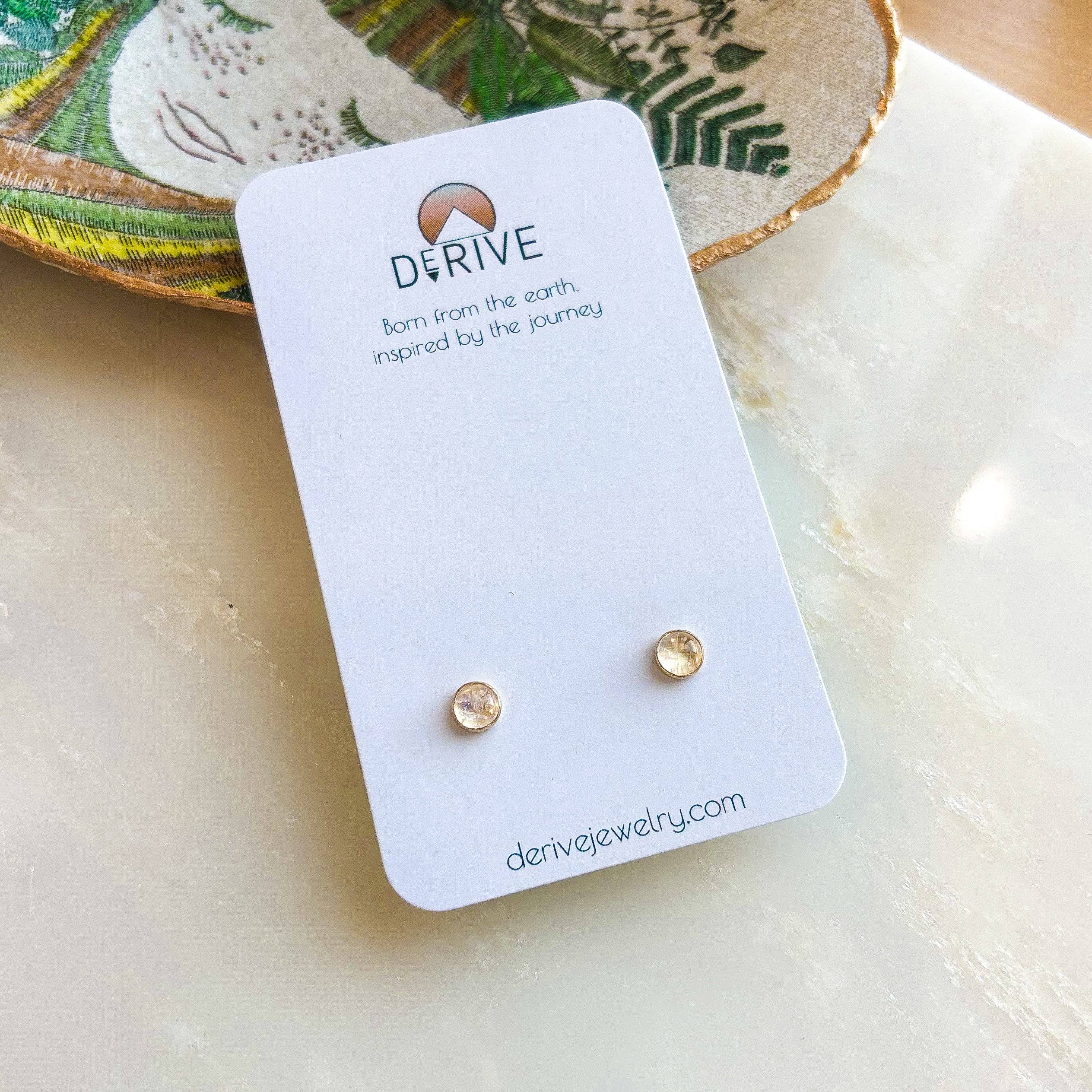 Gemstone Stud Earrings from Derive Jewelry with a delicate Moonstone gemstone showcased on a stylish display card.