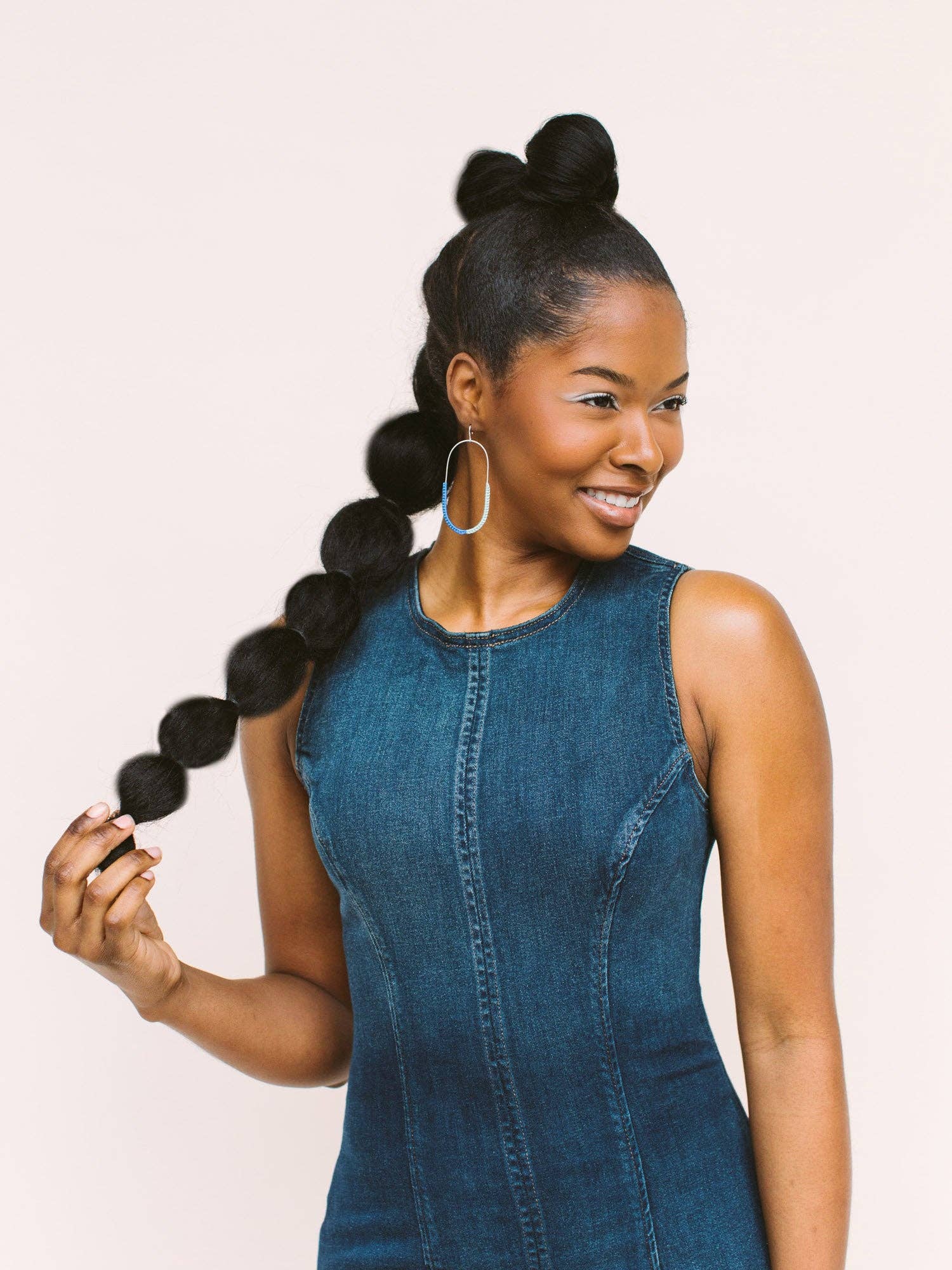 Model showcasing the On the Move Macramé Earrings by Twenty Two West, holding a long braid while smiling.