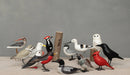 A collection of hand crafted wooden bird ornaments designed by Aviologie, featuring various bird species including the Mini Yellow Legs, showcasing intricate painting and sustainable materials.