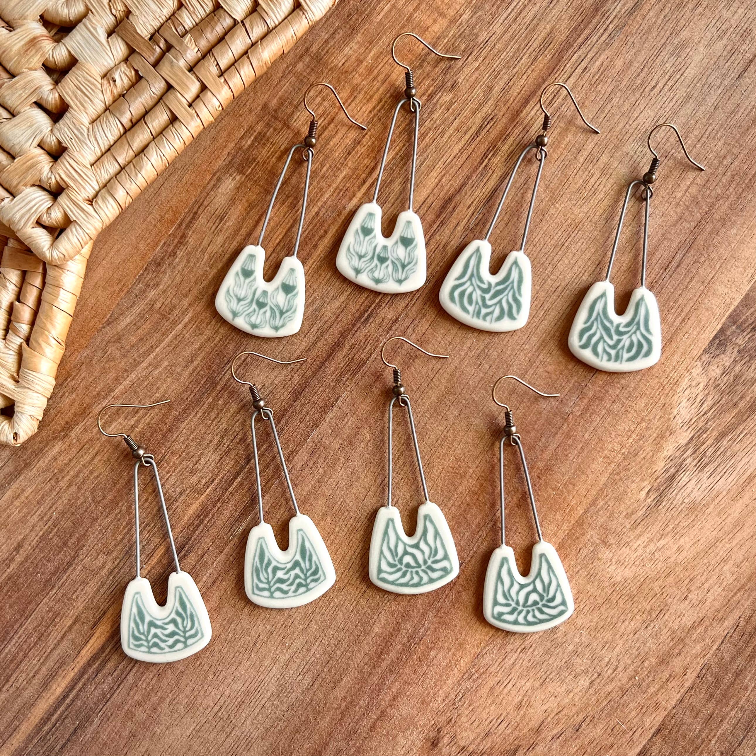 A collection of Teal Negative Space Leafy Earrings by The Artifact House arranged on a wooden surface, highlighting their handcrafted nature and unique designs.