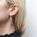 Teardrop with Teardrop Ring Wire Earrings by Marjorie Baer worn on a model's ear, highlighting the contemporary two-tone design and graceful movement of the earrings.