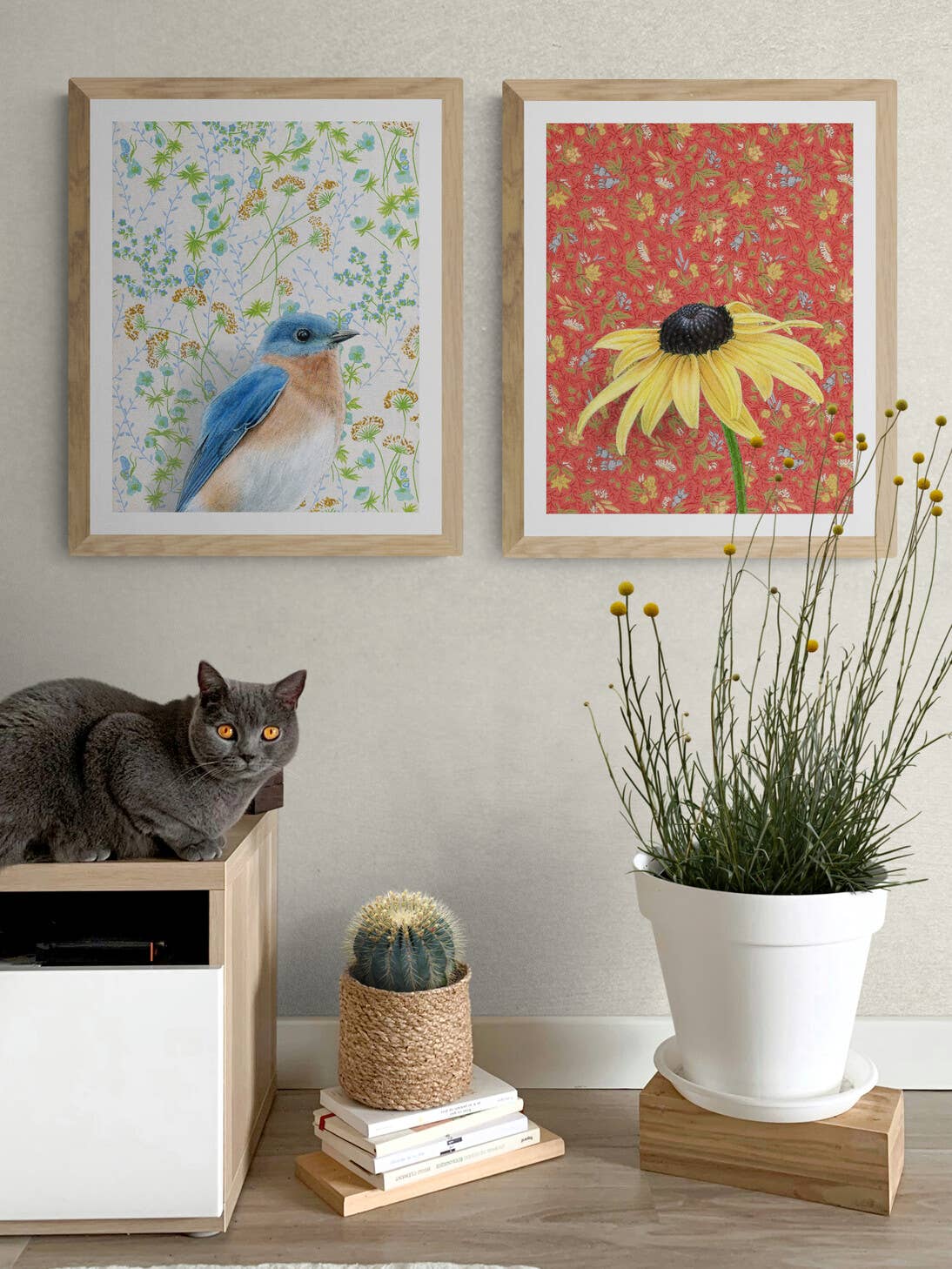 Interior scene showcasing framed art prints titled Bluebird by Emily Uchytil, with a cat sitting beside a plant and decor elements.