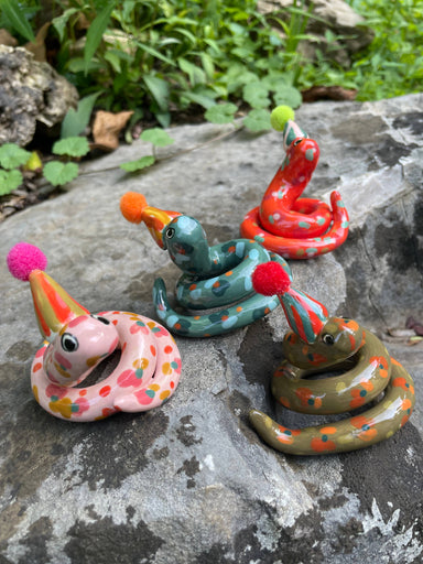 Colorful Itty Bitty Party Snake Sculptures by Bianca Rae, featuring various snakes with party hats and pom poms, showcasing assorted colors and playful designs, perfect for cake toppers or decorative accents.
