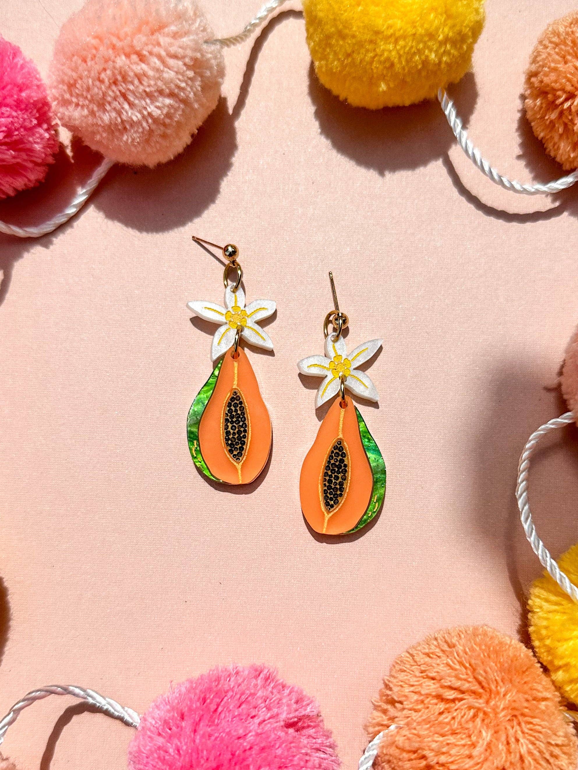 Colorful Papaya Dangle earrings from Sunnie Creative showcased on a pastel backdrop with pom-poms, highlighting their vibrant design and tropical theme.