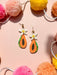 Colorful Papaya Dangle earrings from Sunnie Creative showcased on a pastel backdrop with pom-poms, highlighting their vibrant design and tropical theme.