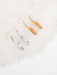 Colorful Skinny Dip Earrings displayed on a bed of white salt, featuring a playful design with vibrant colorways by Twenty Two West.