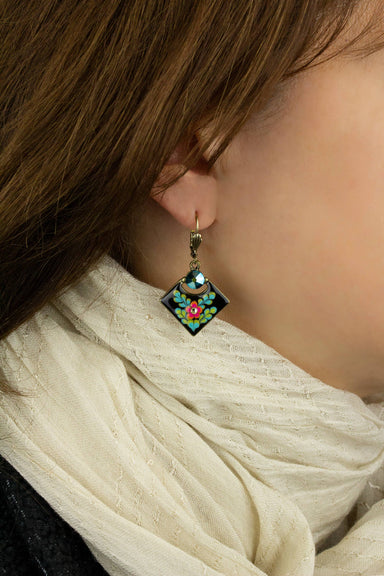 Close-up of a person wearing a floral earring with a white scarf.