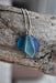 Artistic view of the Sterling Silver Recycled Glass Necklace by Whitelotus Design with three blue frosted glass drops, elegantly clustered on a driftwood display.