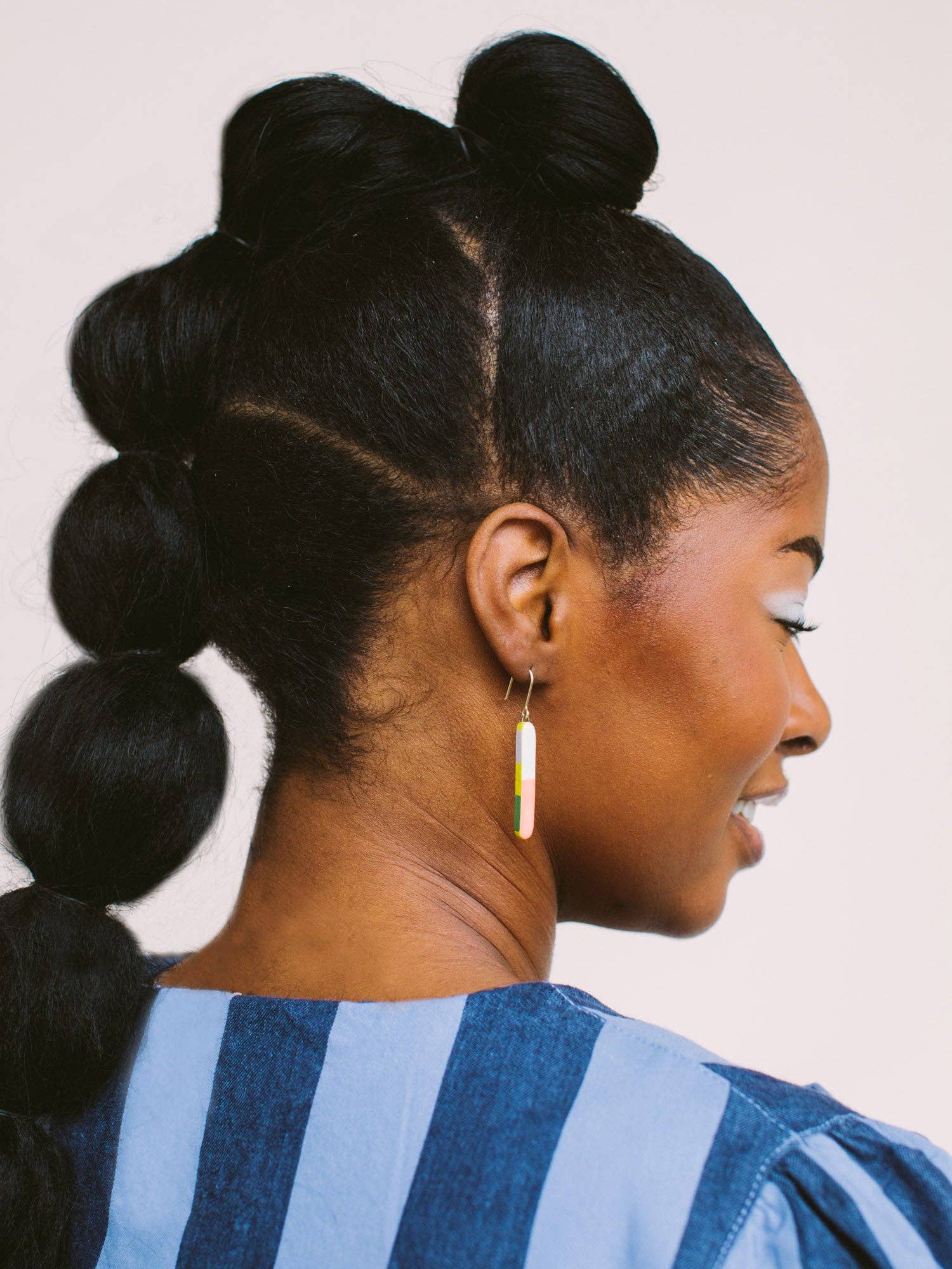 Side profile of a model with long hair, wearing Skinny Dip Earrings that complement the blue striped top, designed by Twenty Two West.